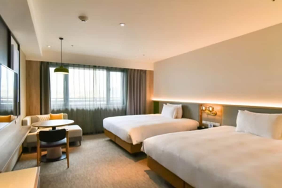 A hotel room with two beds, a desk, a chair, and a window with curtains.
