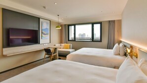 Habitación de hotel con dos camas, un escritorio, una silla, un televisor y un ventanal grande.