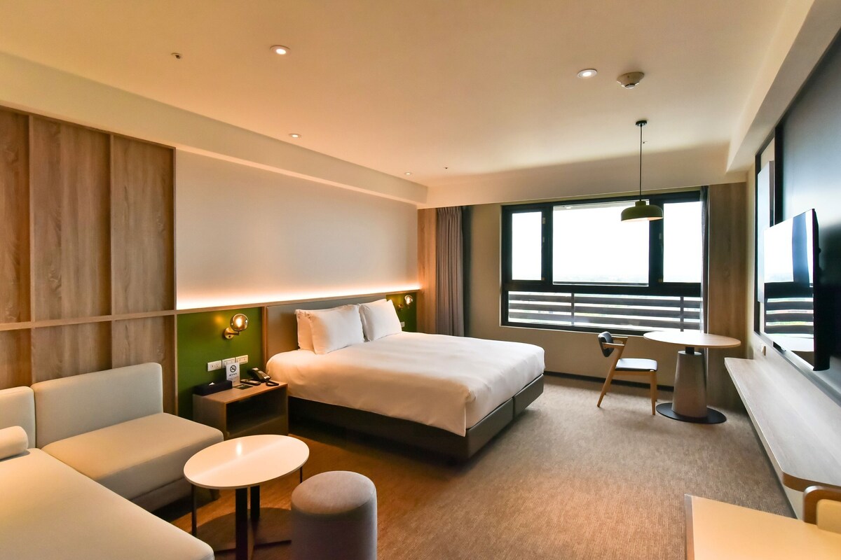 Una habitación de hotel moderna con una cama grande, un sofá, una mesita redonda y un escritorio.