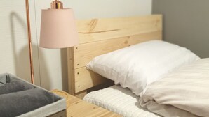 A neatly made bed with white bedding, a wooden bedside table with a lamp, and a small basket. - FILL HOUSE (Seoul)