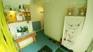 A room with a desk, shelves with plush toys, a welcome banner, and a shoe rack. - FILL HOUSE (Seoul)