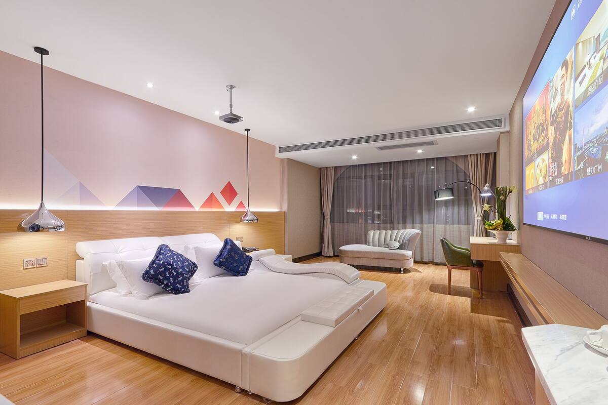 A modern hotel room with a large bed, a desk, a chair, and a TV screen.