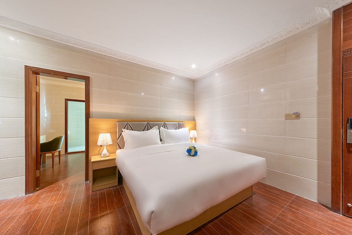 A hotel room with a large bed, wooden floor, and a wooden door.