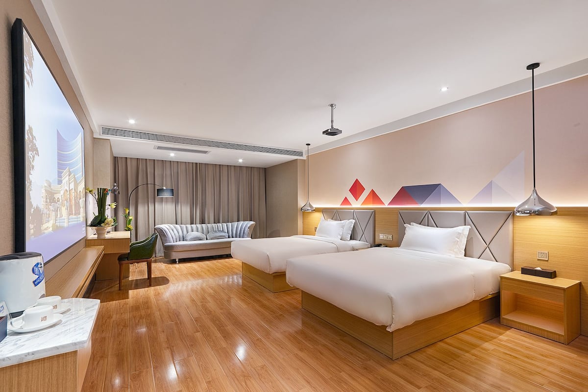 A modern hotel room with two beds, a large window, a flat-screen TV, a coffee station, and a decorative wall with geometric shapes.