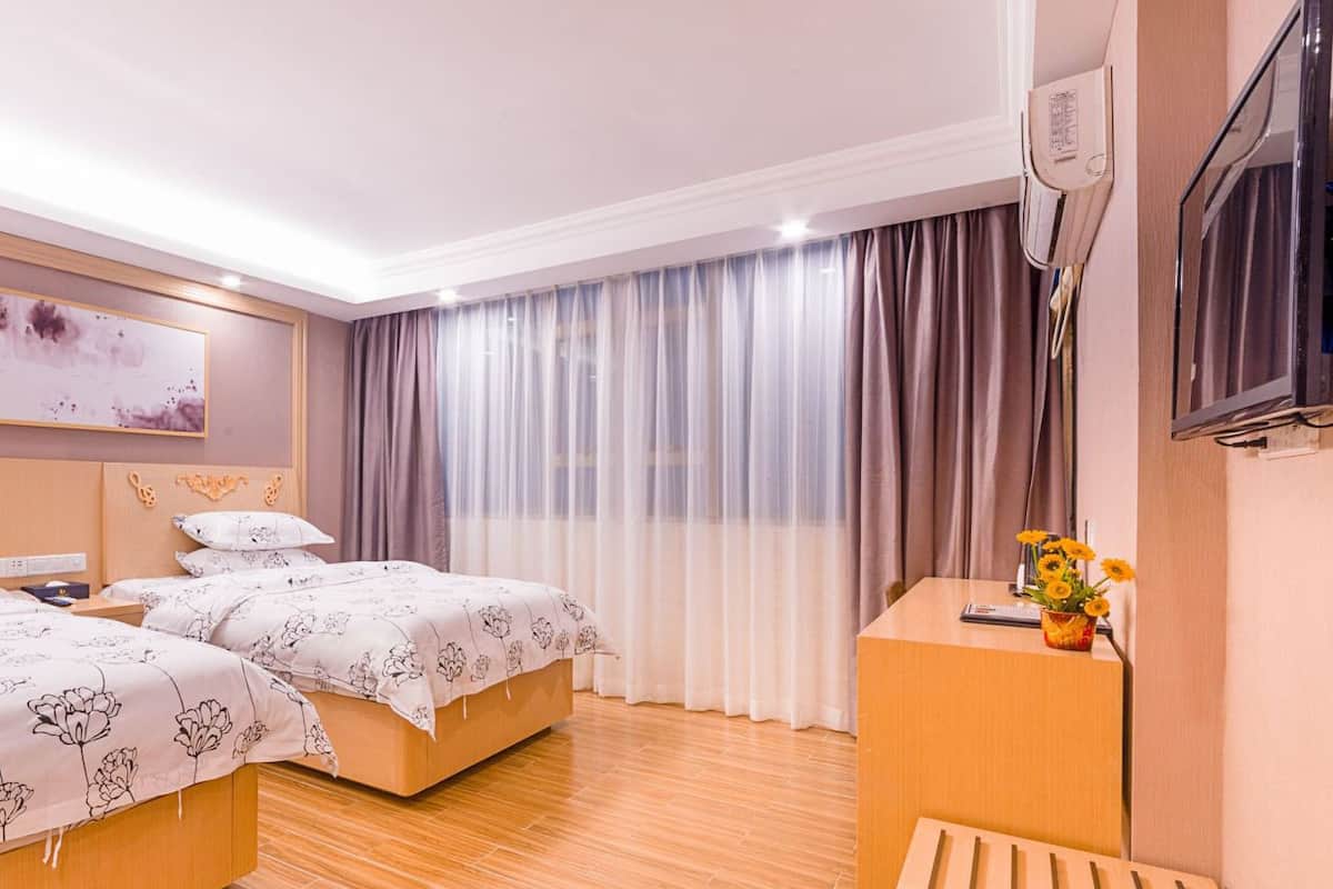 A hotel room with two beds, a wooden desk, a TV, and a window with curtains.