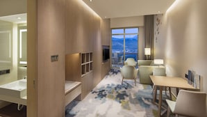 Ein Hotelzimmer mit großem Fenster, einem Flachbildfernseher, einem Schreibtisch und einem Sofa.