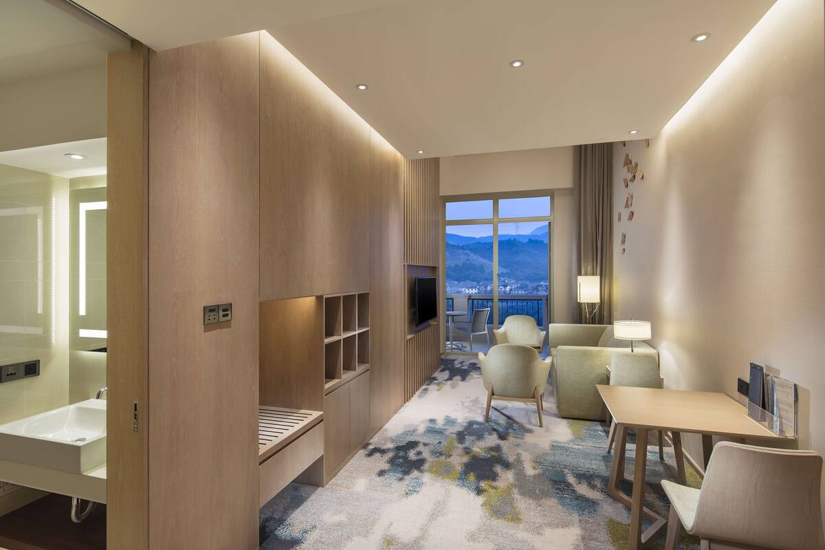 Ein Hotelzimmer mit großem Fenster, einem Flachbildfernseher, einem Schreibtisch und einem Sofa.