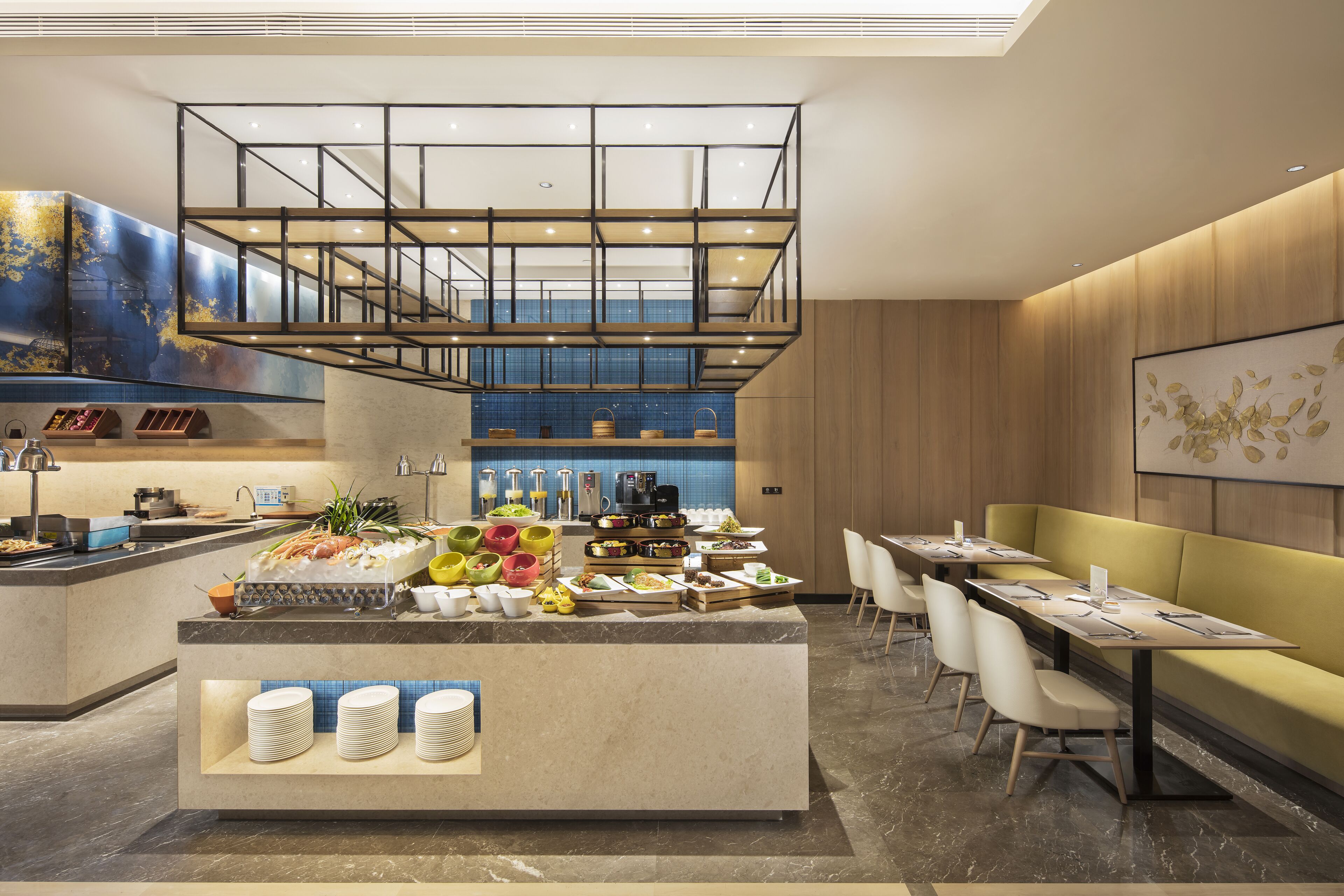 A modern hotel lobby with a central buffet, seating area, and a staircase.