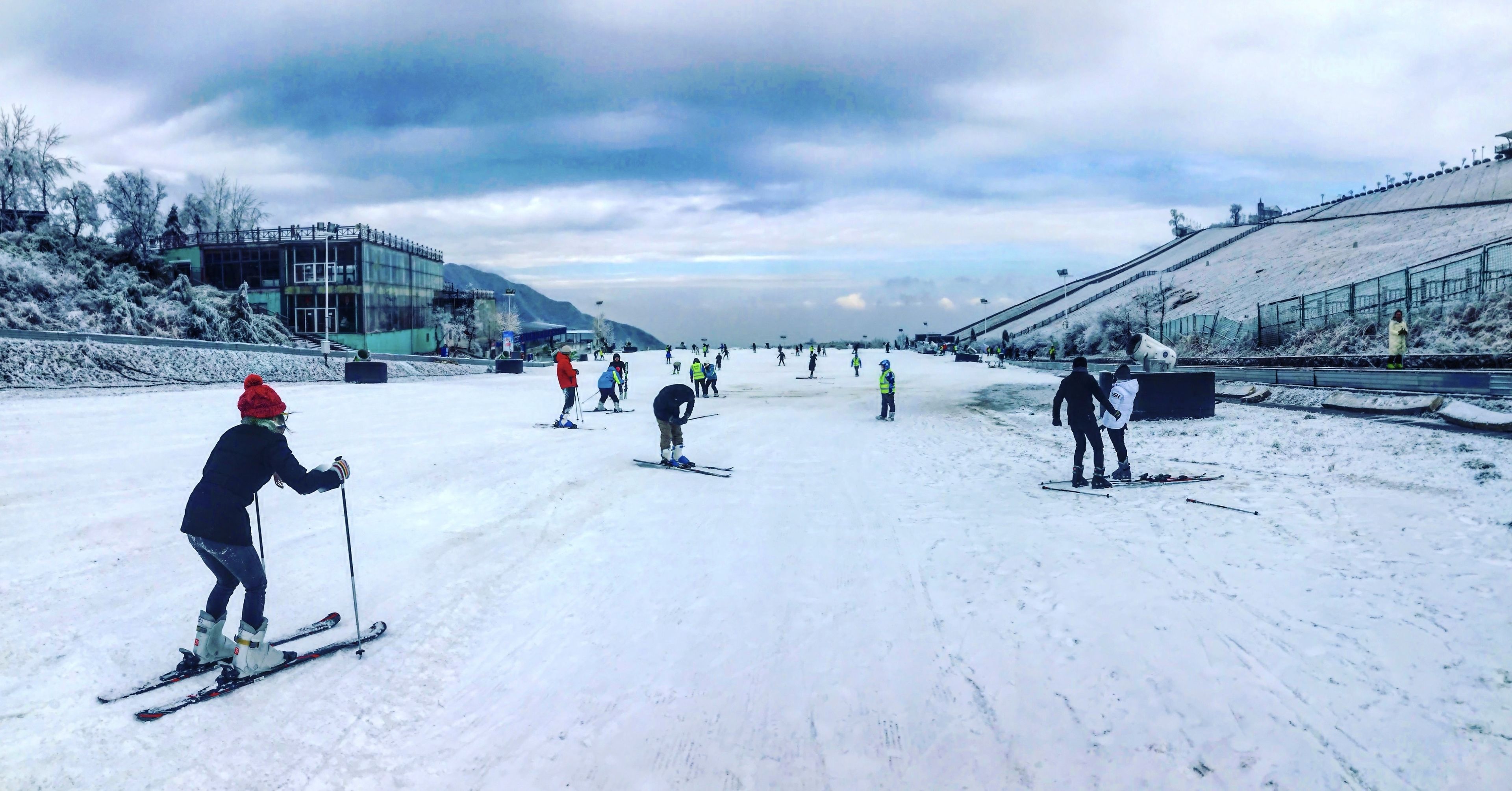 Pista de esquí nevada con esquiadores y un edificio grande al fondo.