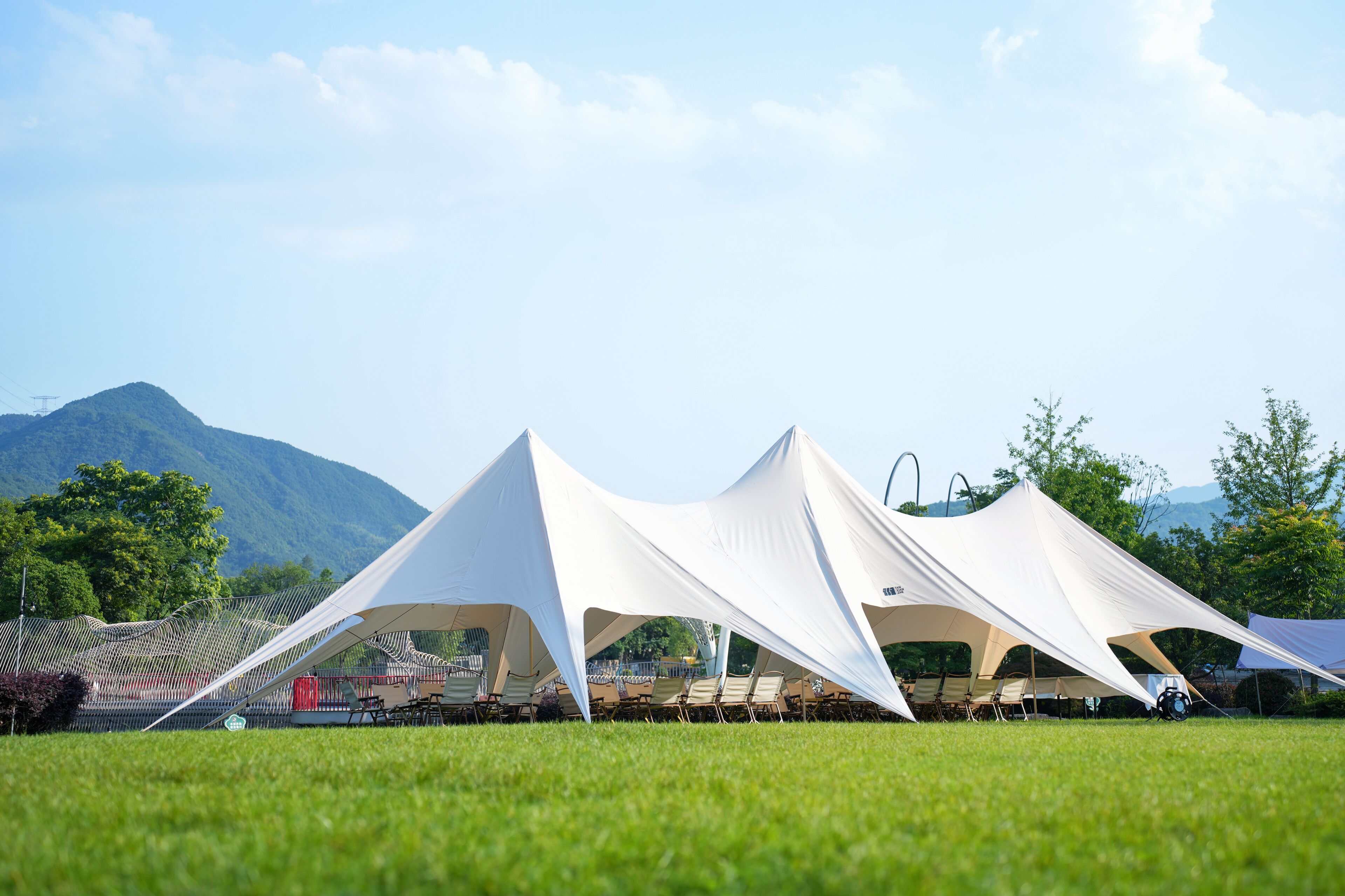 A series of white tents set up on a grassy field with a mountain in the background.