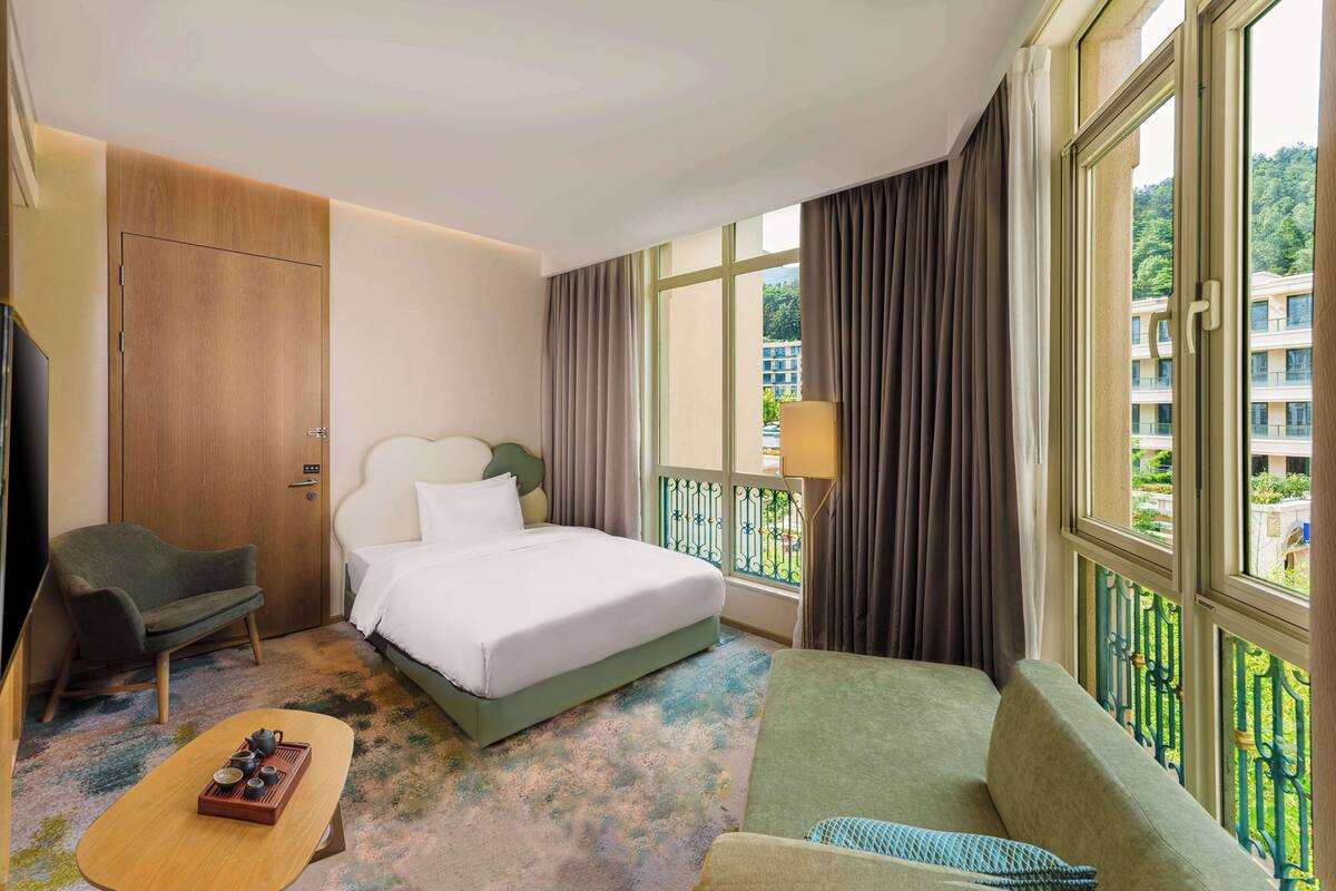 Ein Hotelzimmer mit Bett, einer Couch, einem Sessel, einem kleinen Tisch mit Tablett und einem Fenster mit Vorhängen.