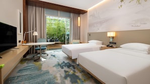 Ein Hotelzimmer mit zwei Betten, einem Schreibtisch mit Stuhl, einem Fernseher und einem Fenster mit Vorhängen.