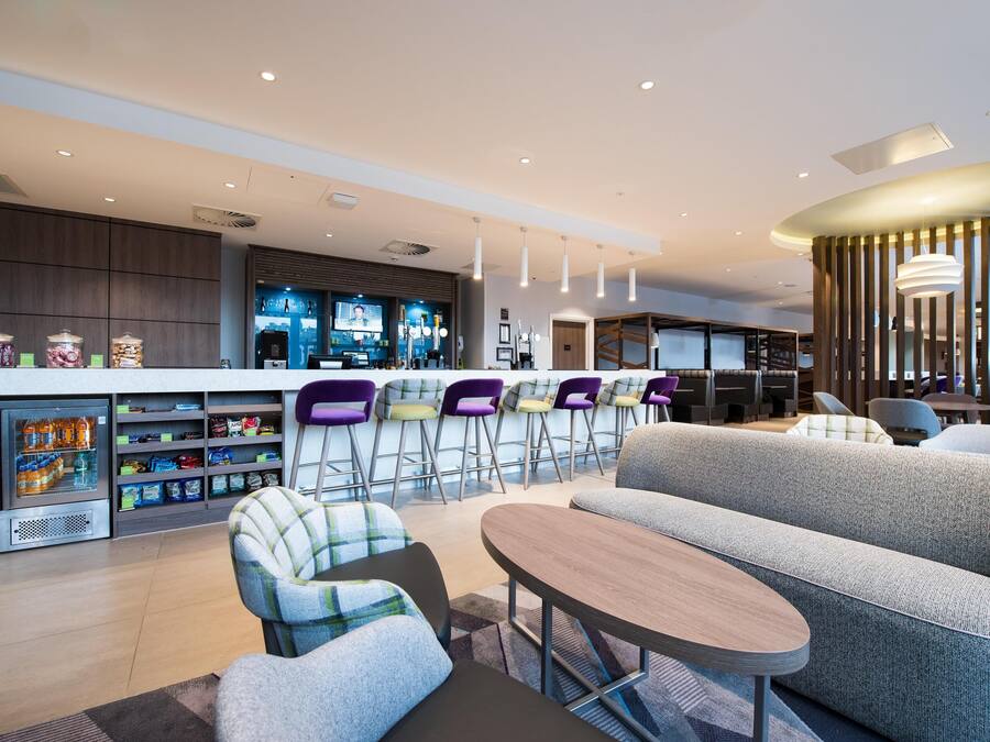 A modern hotel lobby with a bar area, seating, and a refrigerator stocked with beverages.
