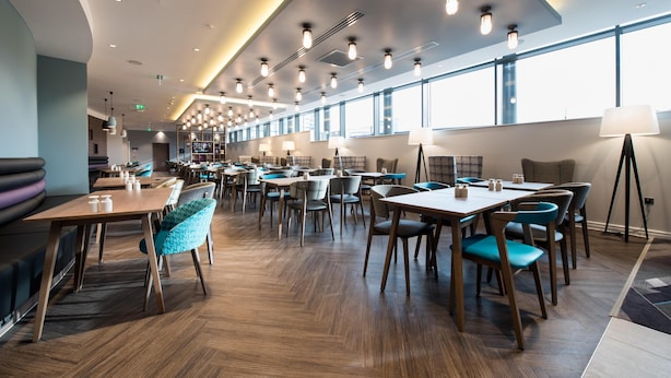 Un restaurante moderno con mesas y sillas de madera, ventanas amplias e iluminación colgante.