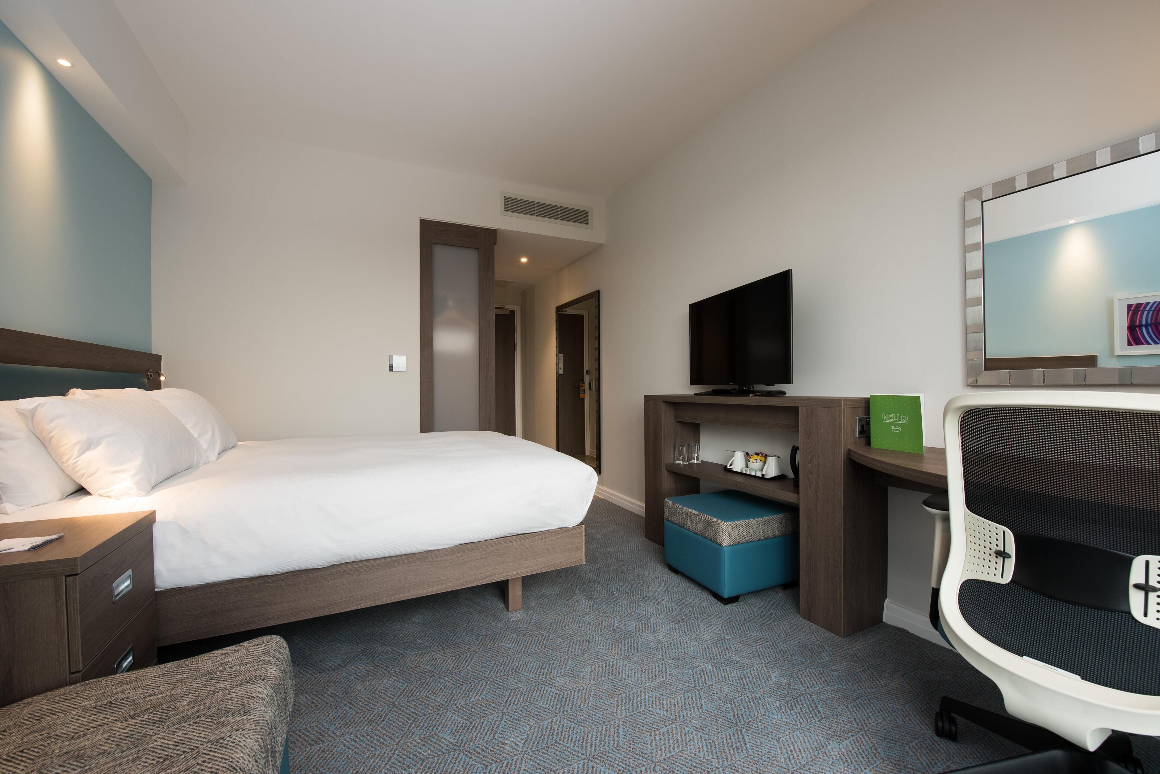 A hotel room with a bed, a desk with a chair, a television, and a small seating area.