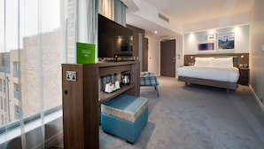 Habitación de hotel con cama, televisión, zona de estar y vistas a la ciudad.