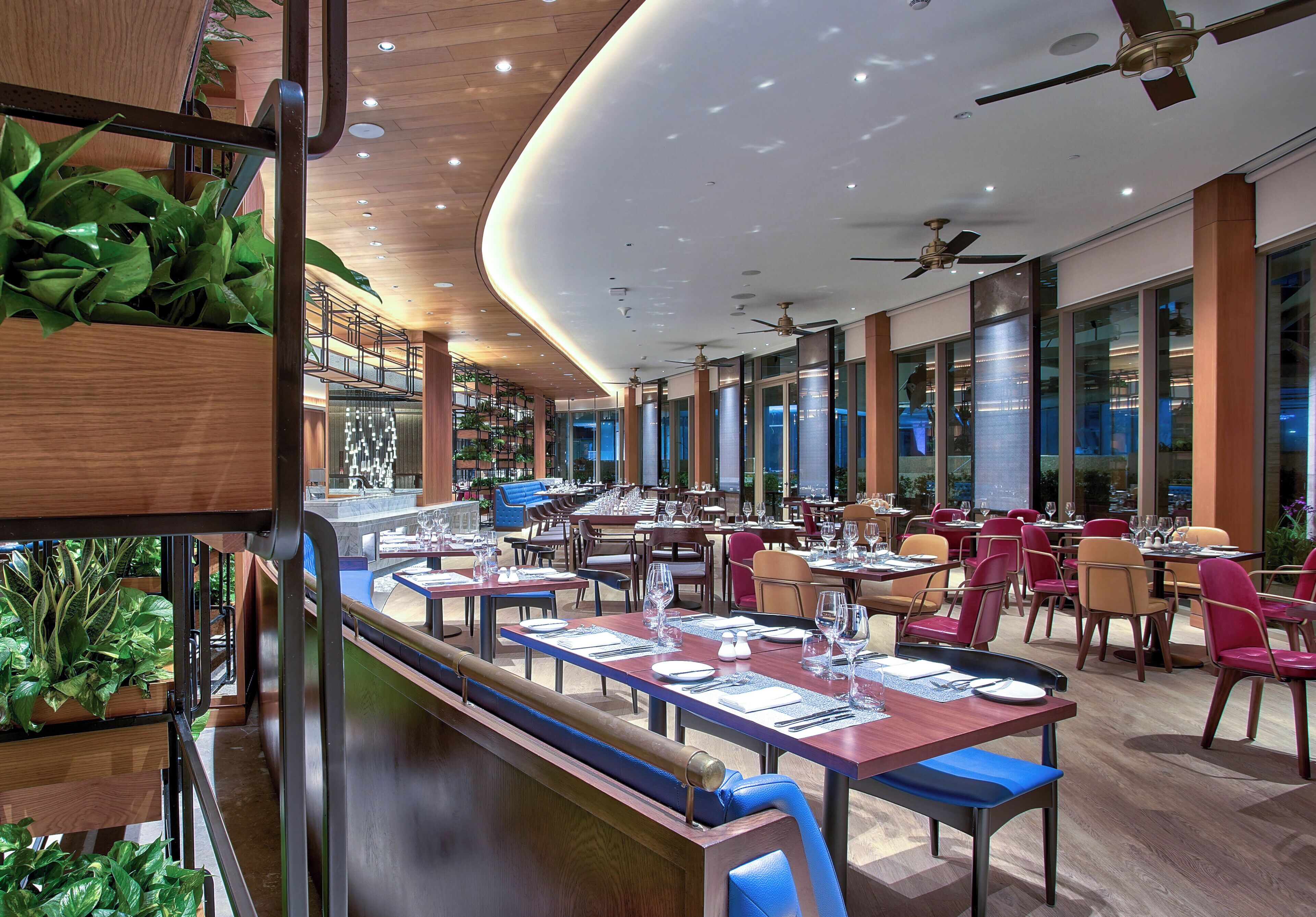 A restaurant with a long counter, multiple tables, chairs, ceiling fans, and large windows.