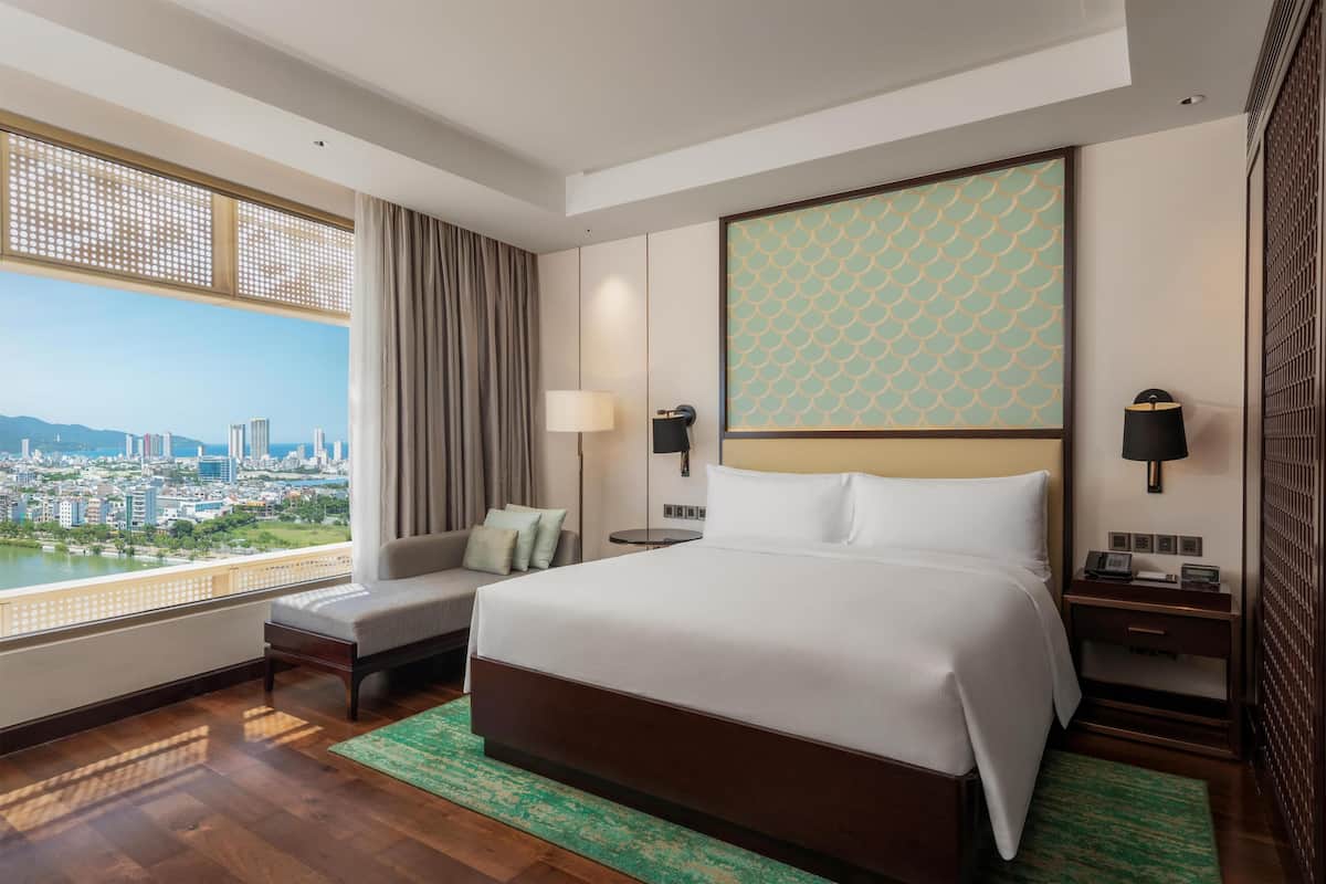 A hotel room with a large bed, a seating area, a view of the city, and a cityscape through the window.