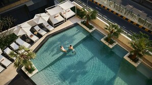 Vista aérea de una piscina con sillones de descanso y palmeras.