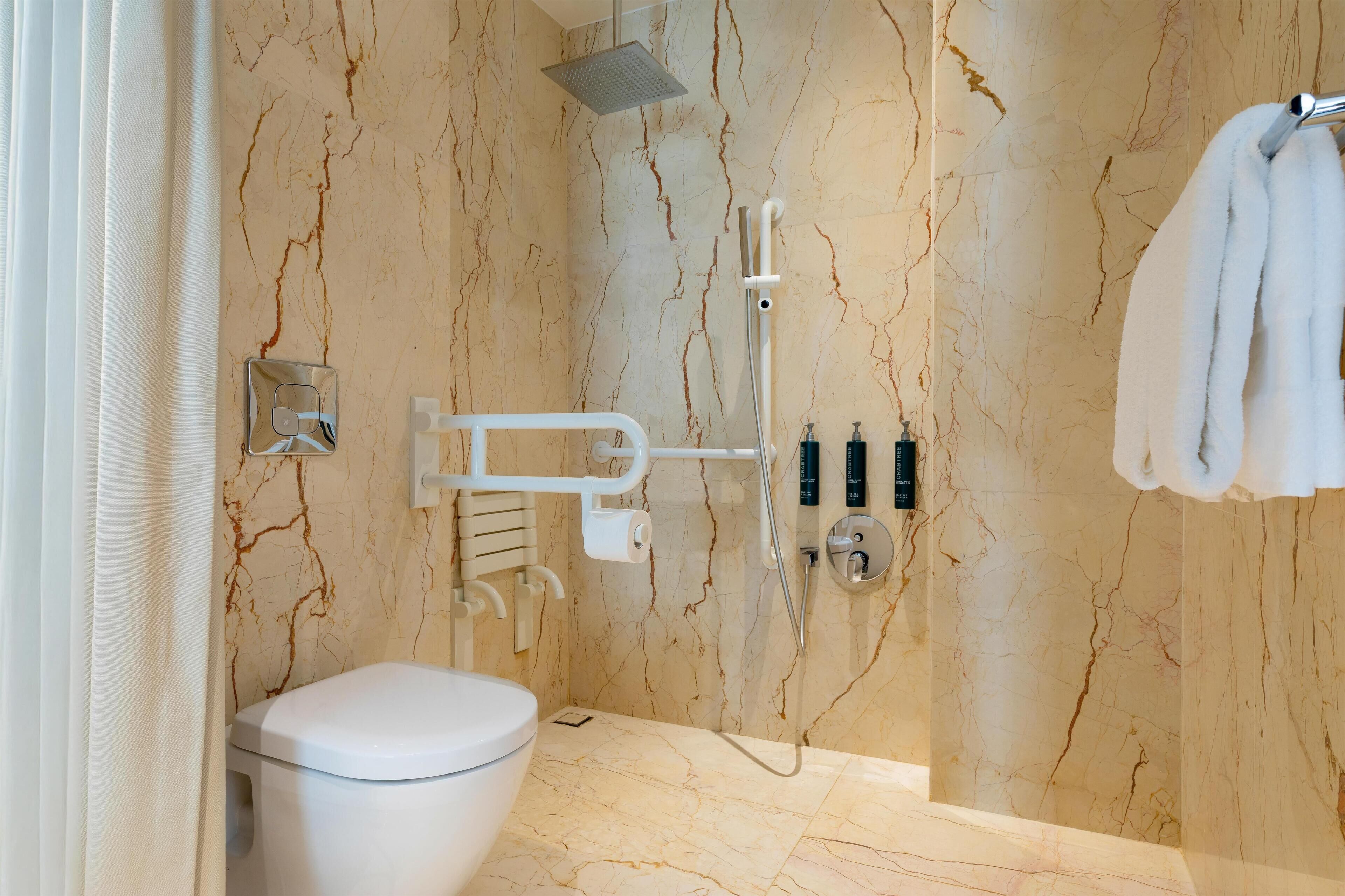 Un baño moderno con inodoro, ducha con cabezal de ducha manual y toallero con toallas.