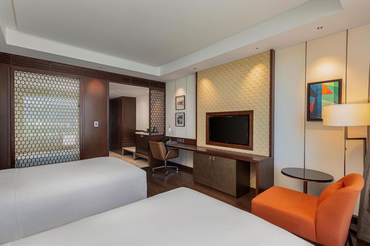 A hotel room with two beds, a desk, a TV, and a lamp.