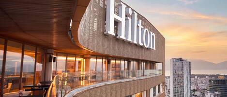 A modern hotel with a prominent 'Hilton' sign, large windows, and a view of the cityscape.