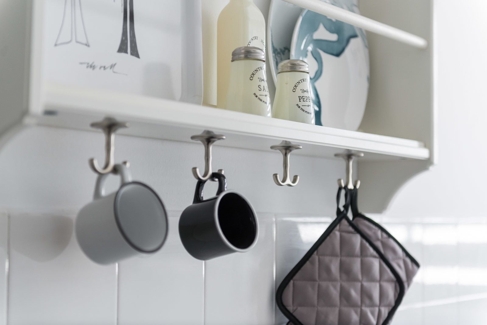 A kitchen with a white tiled backsplash, a shelf with kitchenware, and hanging utensils.