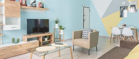 A modern living room with a flat-screen TV, a sofa, a coffee table, and a dining area with chairs.