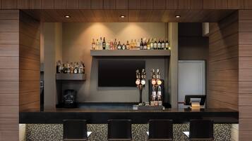 Zona de bar con mostrador, taburetes, una variedad de botellas y una pantalla de televisión.