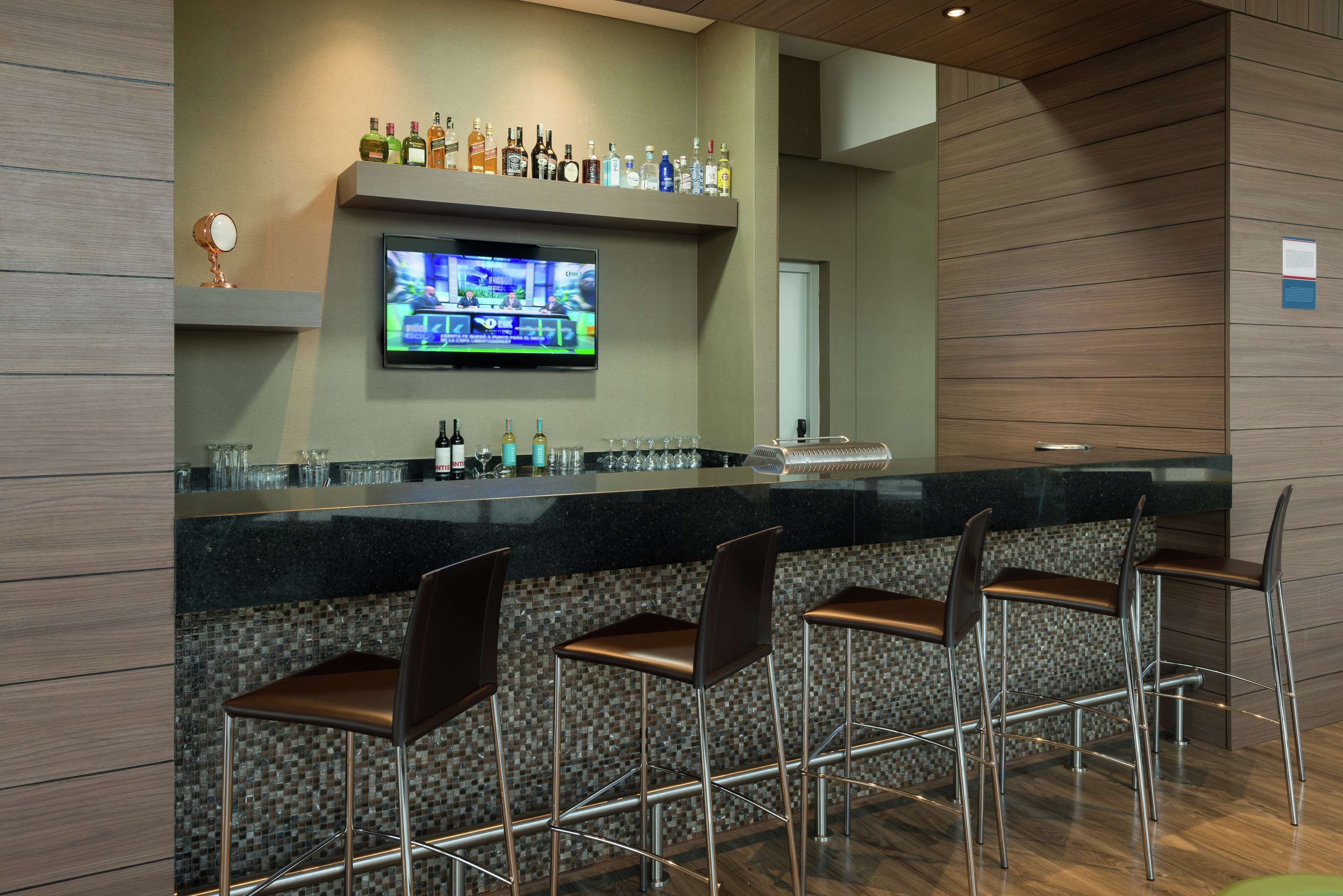 A bar area with a television, bar stools, and a shelf with various bottles.