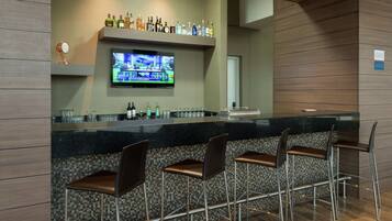 A bar area with a television, bar stools, and a shelf with various bottles.