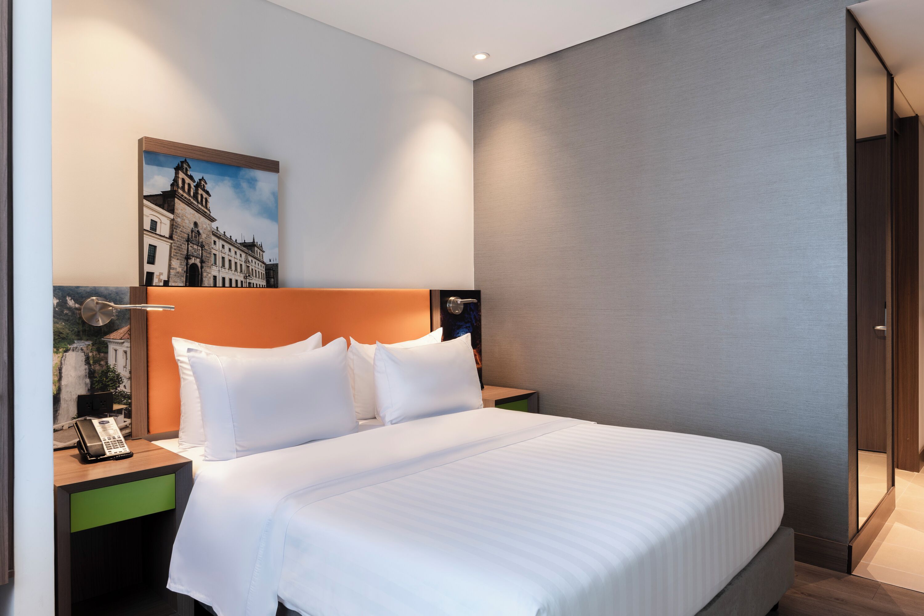 Una habitación de hotel con una cama grande, una mesita de noche con teléfono y un cuadro en la pared.