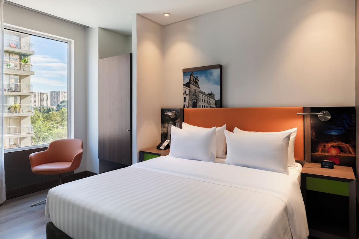 Une chambre d’hôtel moderne avec un grand lit, une chaise, une table de chevet avec un téléphone et un tableau au mur.