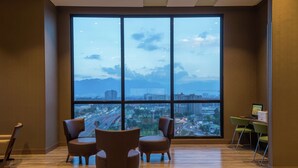 A spacious room with a large window offering a city view, a desk with a computer, and two chairs. - Hampton by Hilton Bogota Airport (Bogotá)