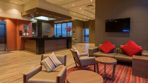 A modern hotel lobby with a reception desk, leather sofas, a TV, and a large window offering a view. - Hampton by Hilton Bogota Airport (Bogotá)