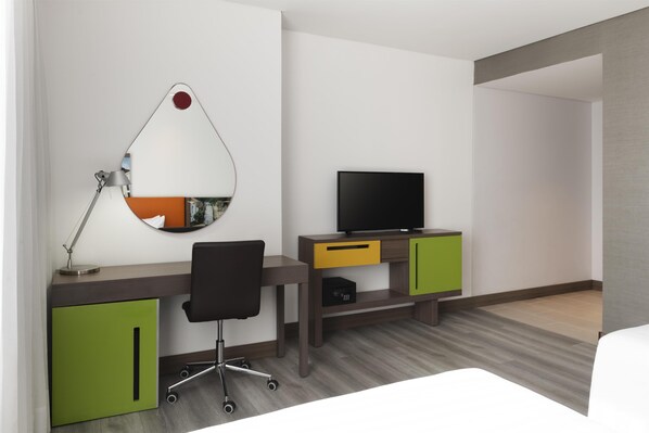 A hotel room with a desk, chair, TV, and a bed.