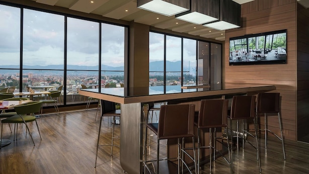 A modern bar area with a large window overlooking a cityscape and mountains. - Hampton by Hilton Bogota Airport (Bogotá)