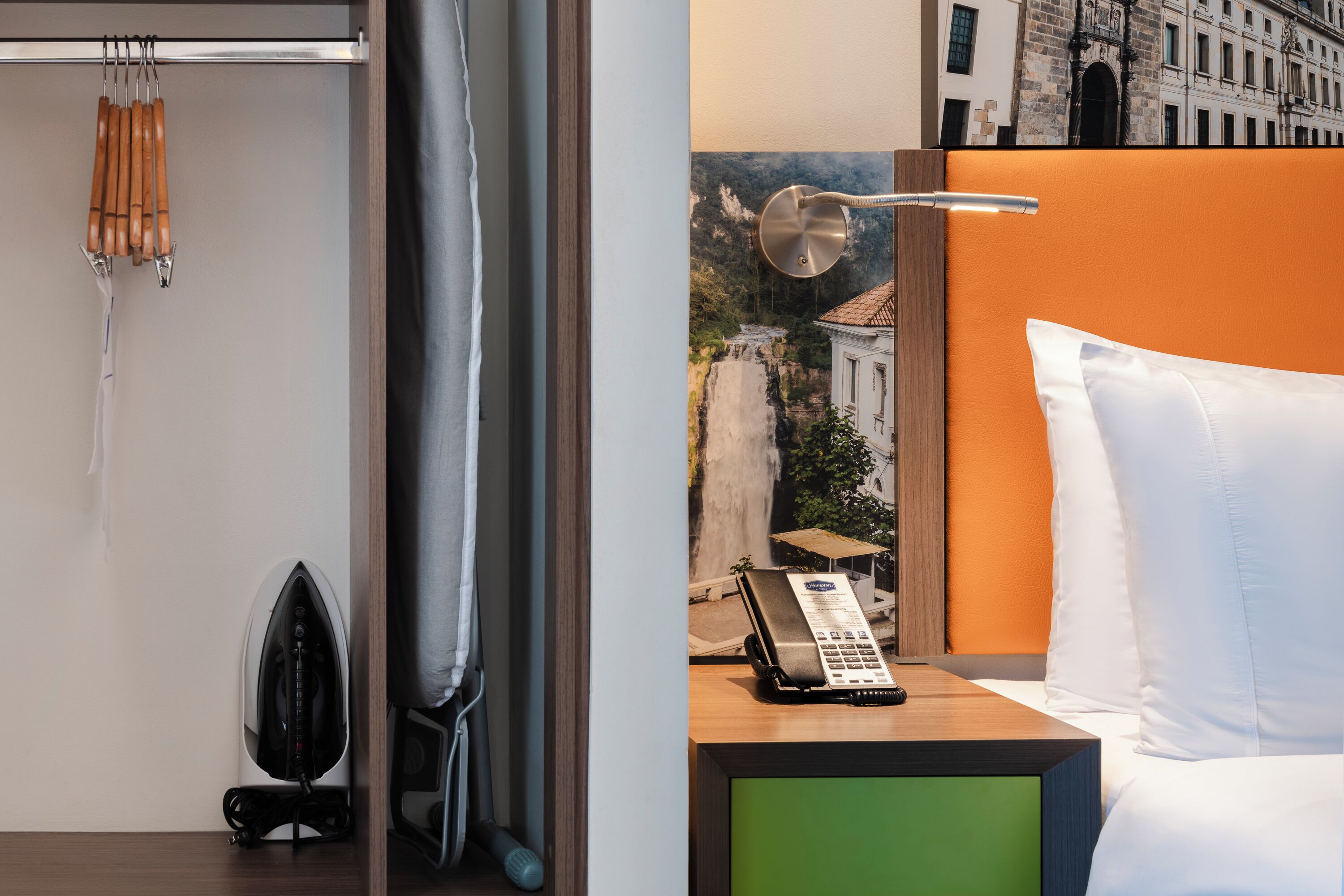 Habitación de hotel con cama, mesita de noche con teléfono, plancha fijada a la pared y cortina de ducha.