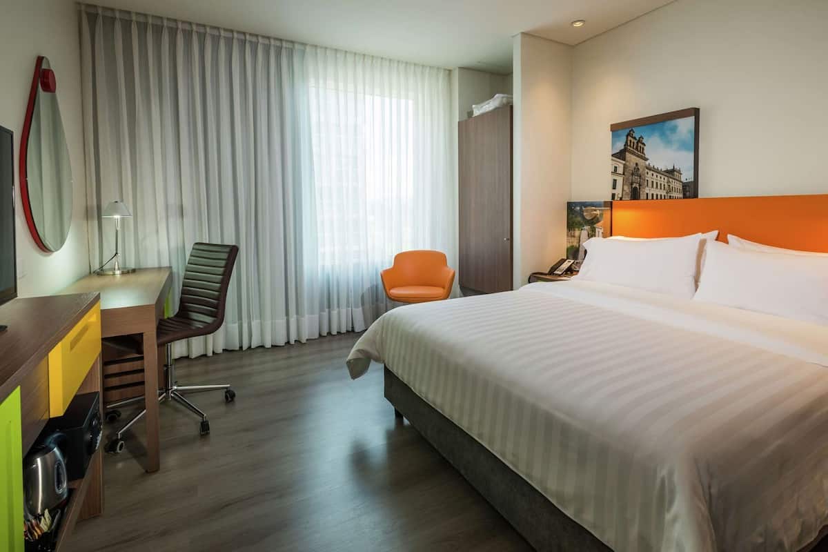 Une chambre d’hôtel avec un lit, un bureau, une chaise et un tableau au mur.