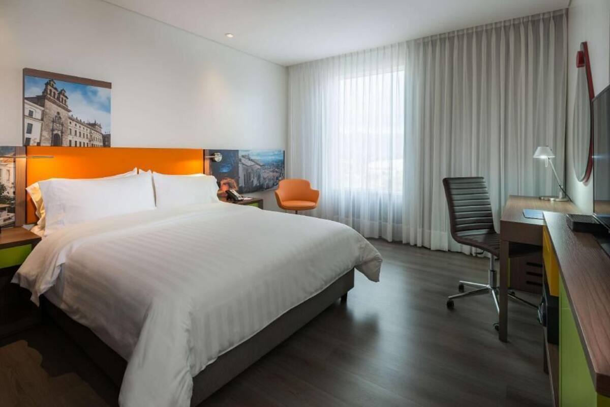 Une chambre d’hôtel avec un grand lit, un bureau avec une chaise, une télévision et une fenêtre avec des rideaux.