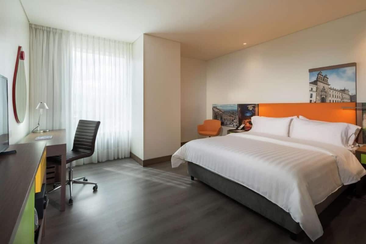 Une chambre d’hôtel avec un lit, un bureau, une chaise et un tableau au mur.
