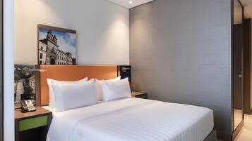 A hotel room with a large bed, a nightstand with a phone, a painting on the wall, and a door to the right.