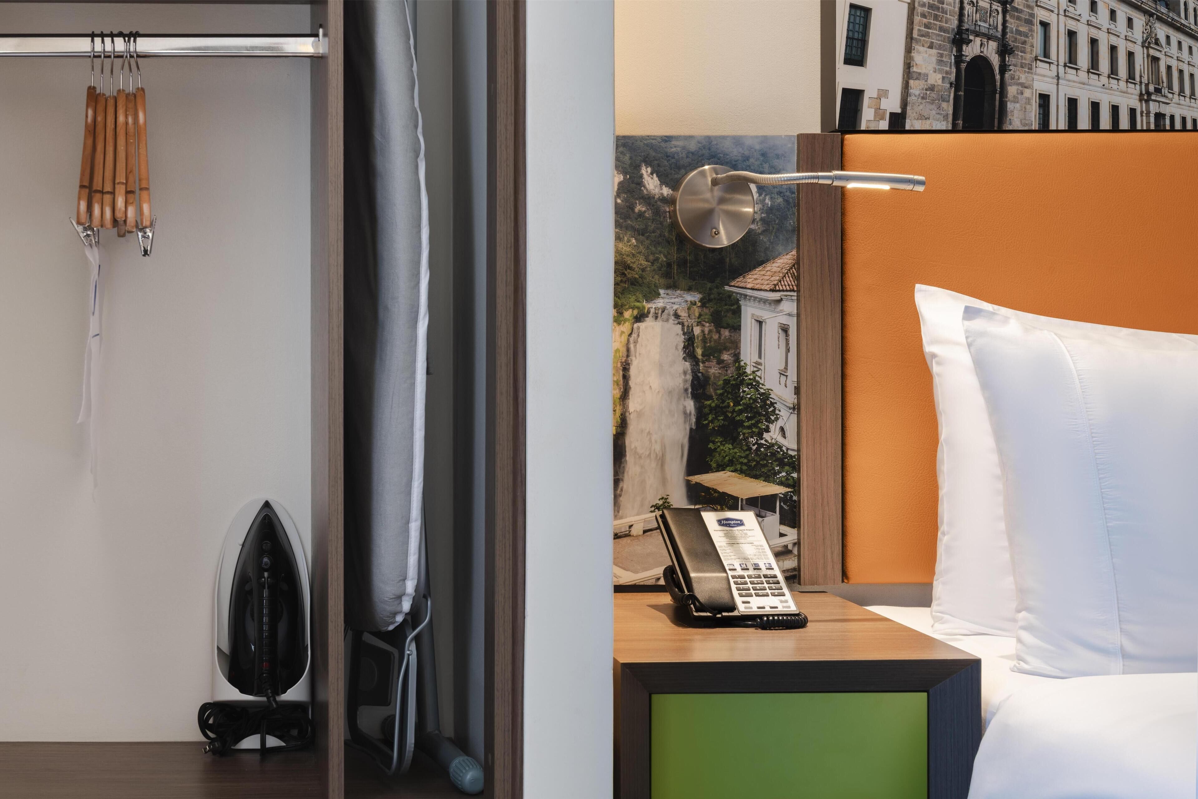 Camera d'albergo con un letto, un telefono, un pannello verde, un quadro che raffigura una cascata e un angolo doccia con porta asciugamani.