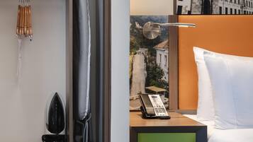 Camera d'albergo con un letto, un telefono, un pannello verde, un quadro che raffigura una cascata e un angolo doccia con porta asciugamani.