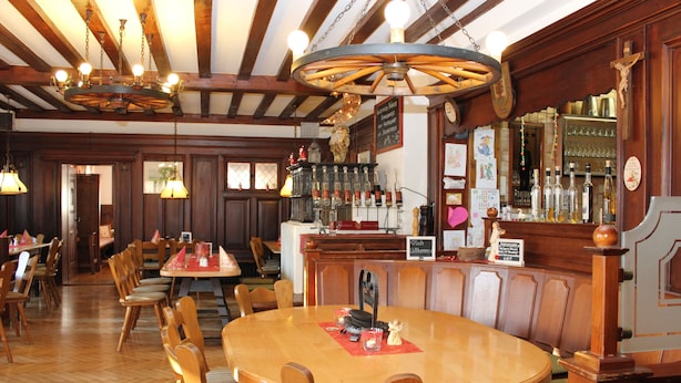 A restaurant with wooden tables and chairs, a bar area with bottles, and a chandelier.