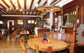 Um restaurante com mesas e cadeiras de madeira, um espaço de bar com garrafas e um candelabro.