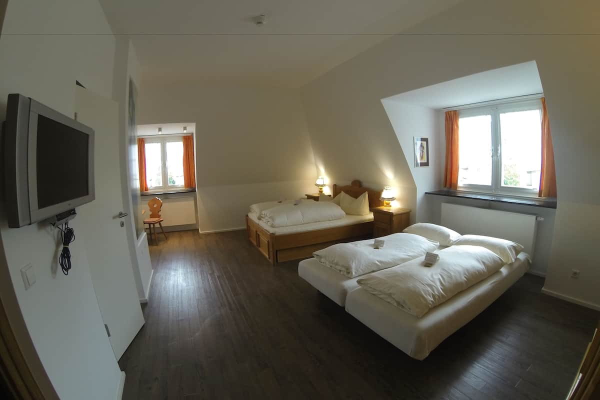 Une chambre avec deux lits, un téléviseur fixé au mur et une fenêtre avec des rideaux.