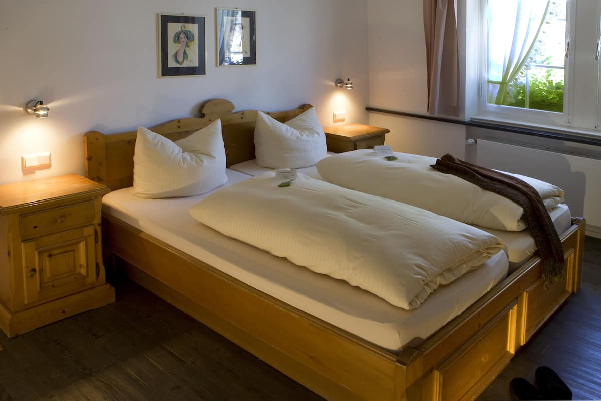 Un lit double avec une tête de lit et un pied de lit en bois, deux tables de chevet et une fenêtre avec des rideaux.