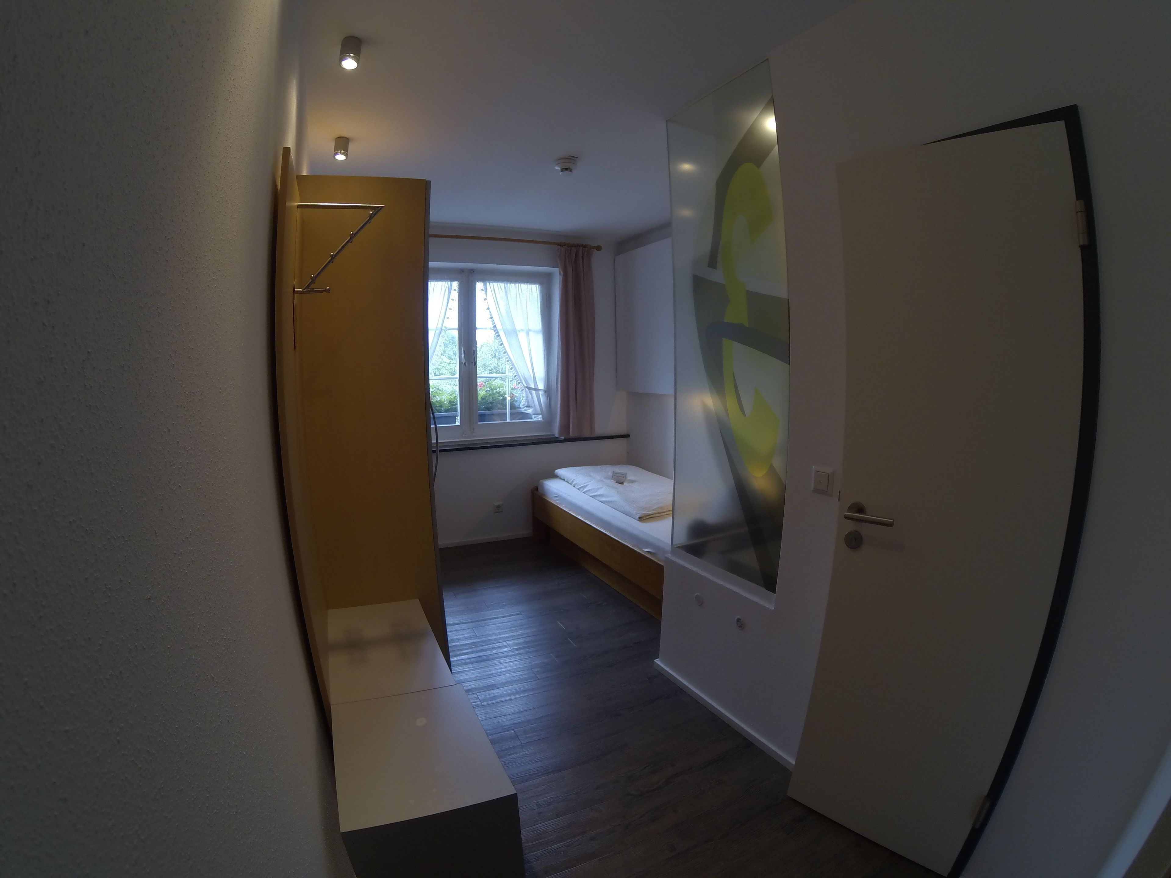 A narrow hallway leading to a room with a bed, a window, and a door.