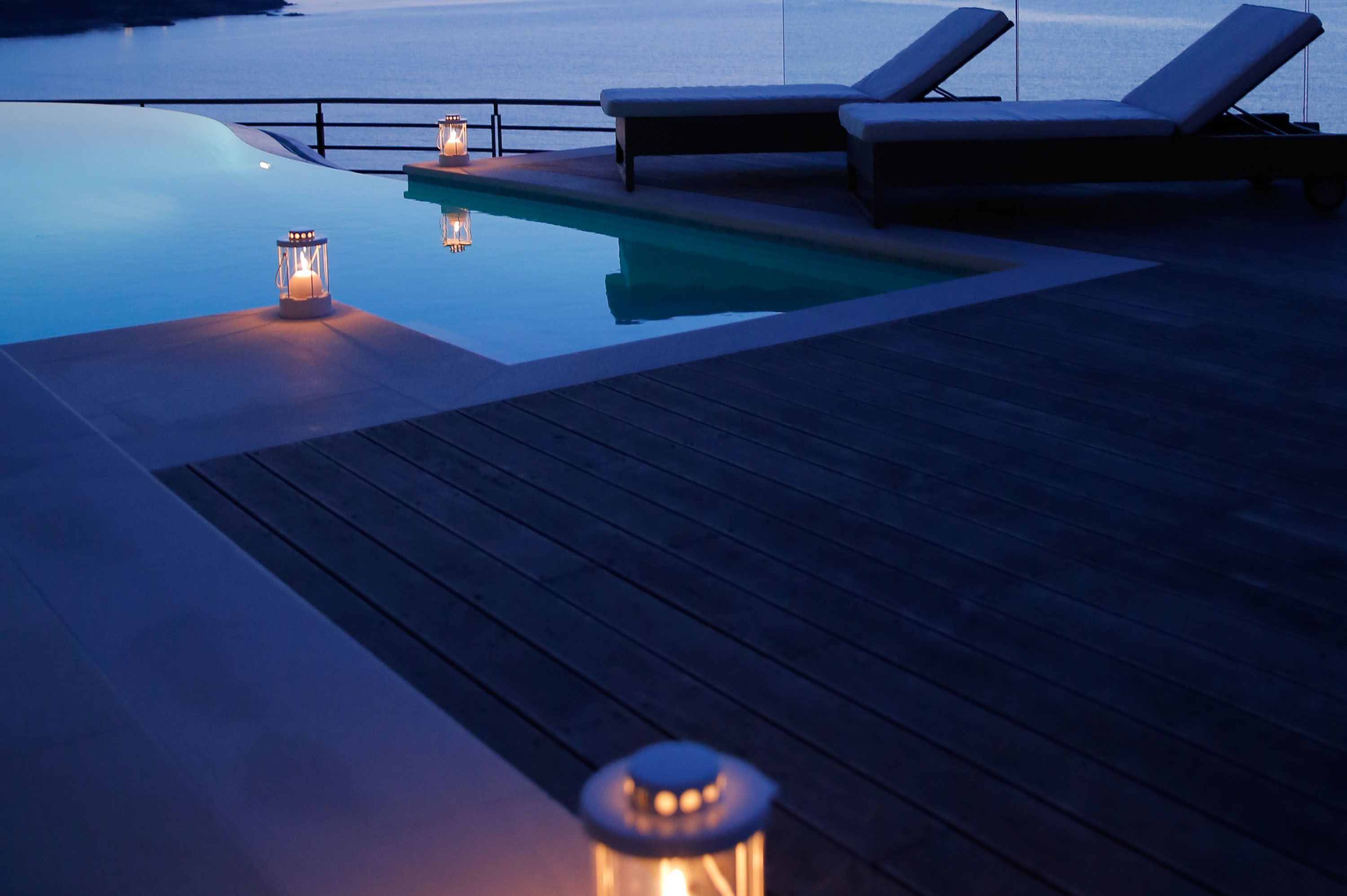 A poolside area with lounge chairs and lanterns, overlooking a calm body of water.